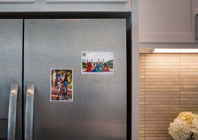 Close up of stainless steel refrigerator with 4 by 6 inch  magnetic photo pocket frames containing images of kids at play.